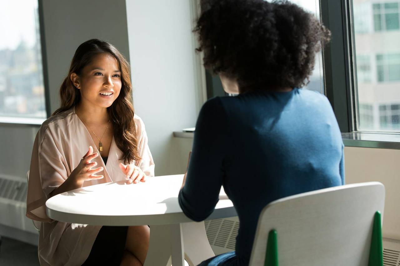 Two women in conversation across a small table in a bright office