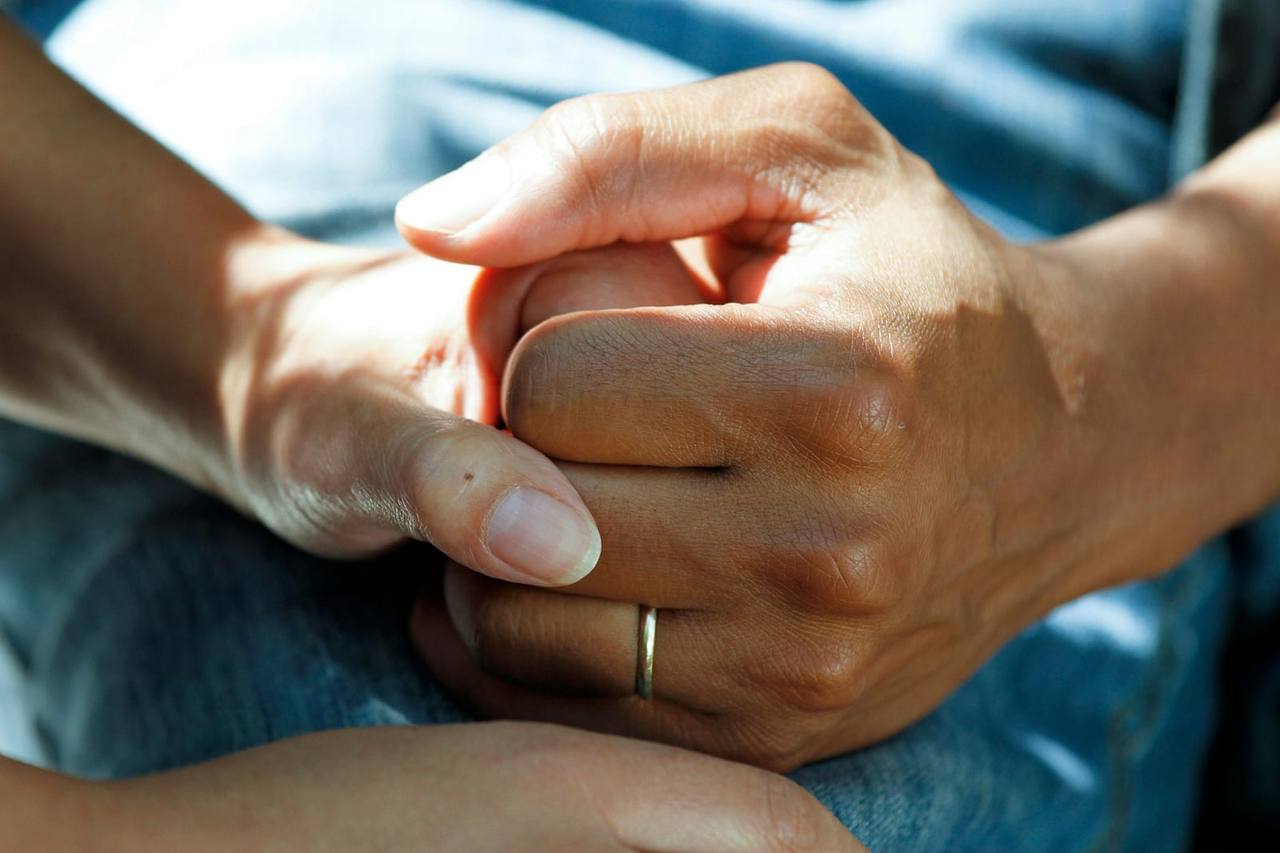 Close-up of a care professional’s hands holding an older person’s hand